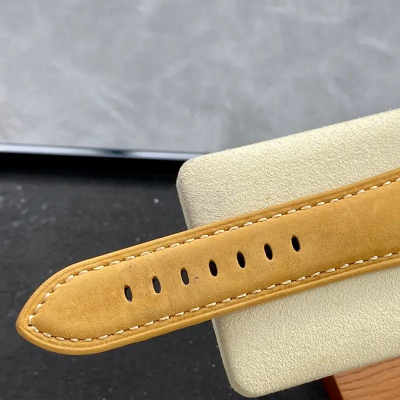 Tan strap end with stitched edges draped over a cream stand
