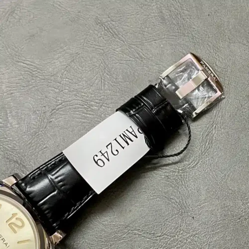 Polished buckle in film beside the strap tag on a grey leather mat