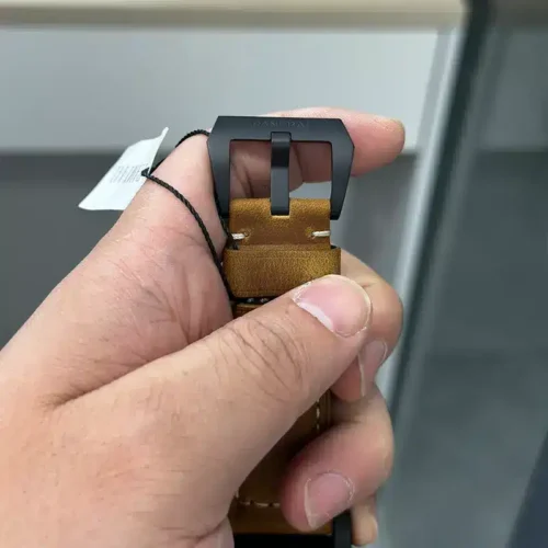 Black tang buckle through the caramel leather, hang tag in the fingers