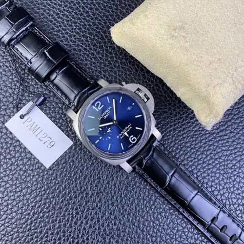 Whole watch laid on dark leather beside its paper tag and cream cushion