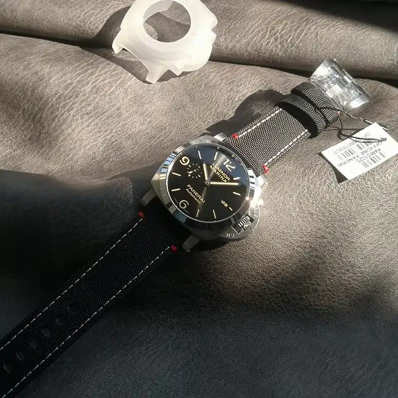Watch on grey leather in sunlight beside a clear case guard and tag