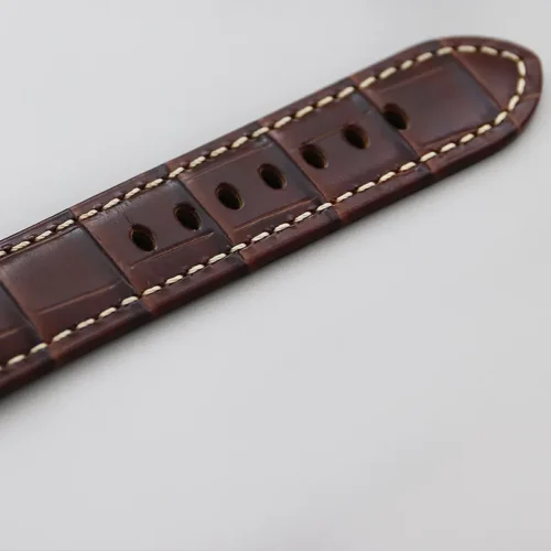 Rounded end of the brown strap with croc grain and thick cream stitching