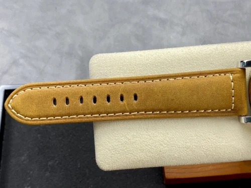Tan leather tail laid over a pale cushion, cream thread along the edge
